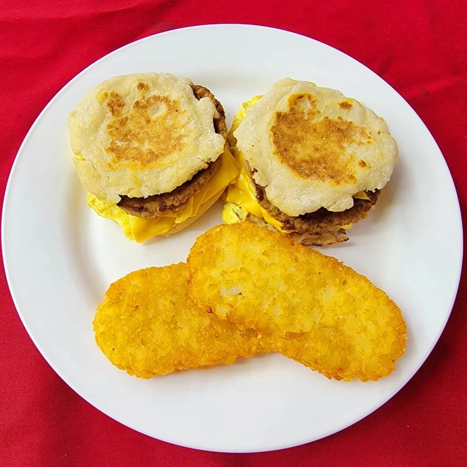 Two breakfast sandwiches with egg, cheese, and sausage patties, alongside two golden hash browns.