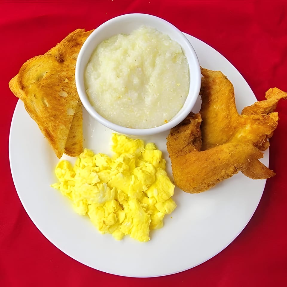 Breakfast plate with scrambled eggs, grits, toast, and fried chicken wings on a red background.