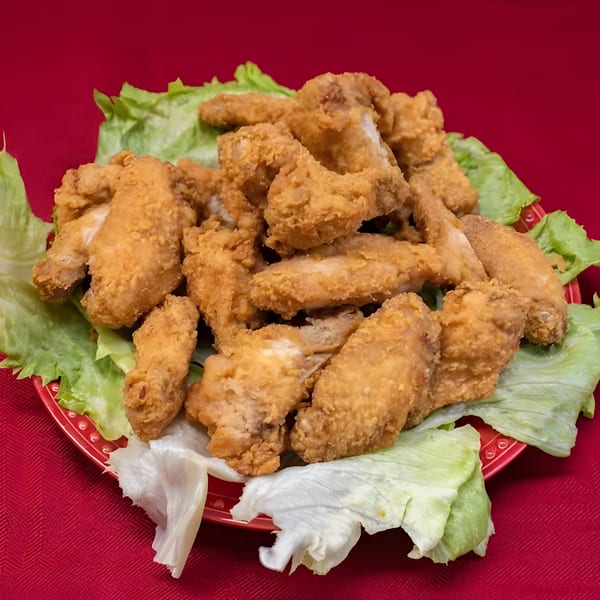 A red plate piled high with golden-brown fried chicken wings and fresh green lettuce.