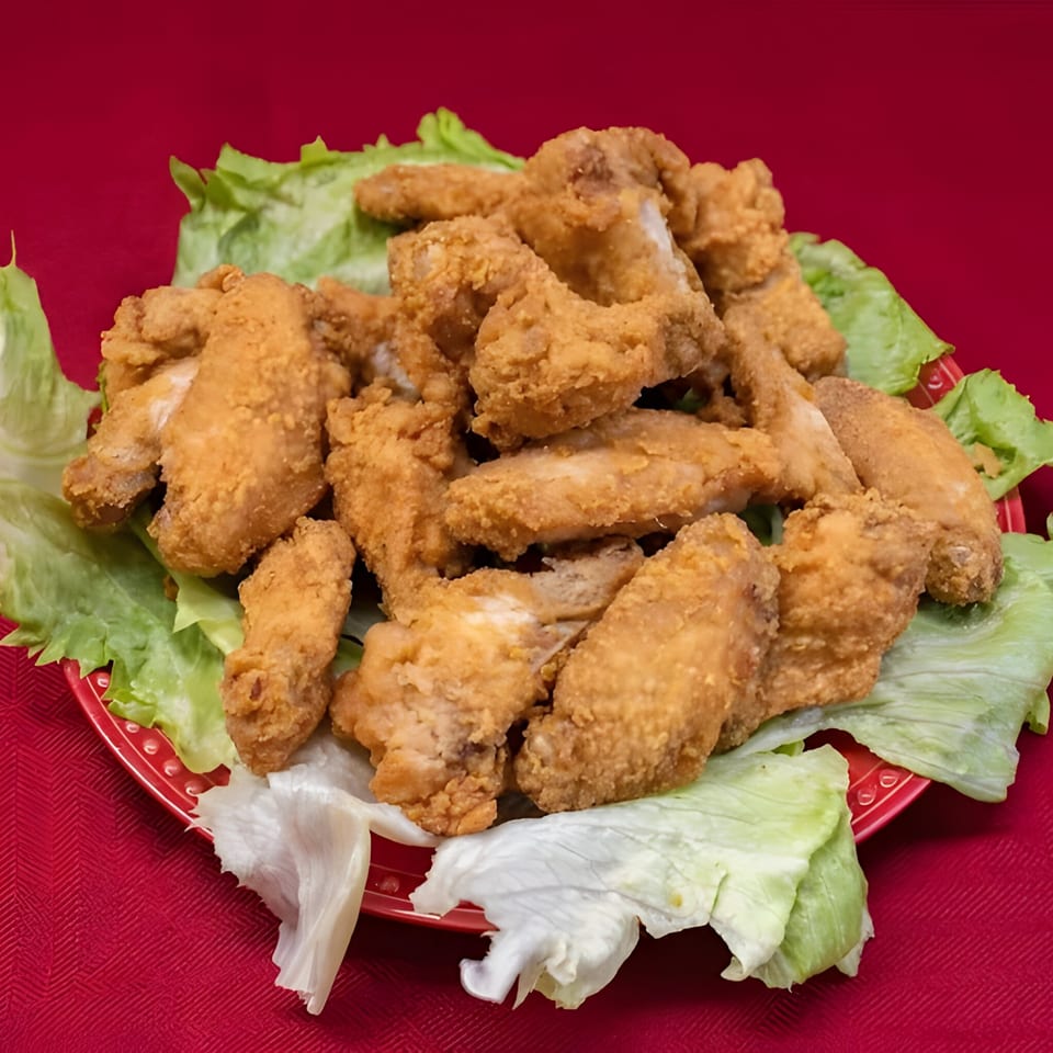 A red plate filled with crispy fried chicken wings and fresh green lettuce on a red tablecloth.