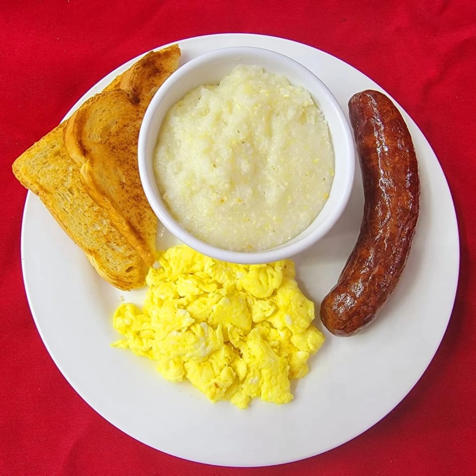 A breakfast plate with scrambled eggs, a sausage link, grits, and two slices of toast.